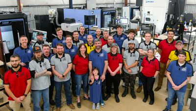 Team photo of Final Frontier Manufacturing crew members in branded shirts on the factory floor, including mascot Mike Rometer