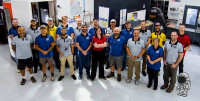 Team photo of Final Frontier Manufacturing crew members in branded shirts on the factory floor, including mascot Mike Rometer